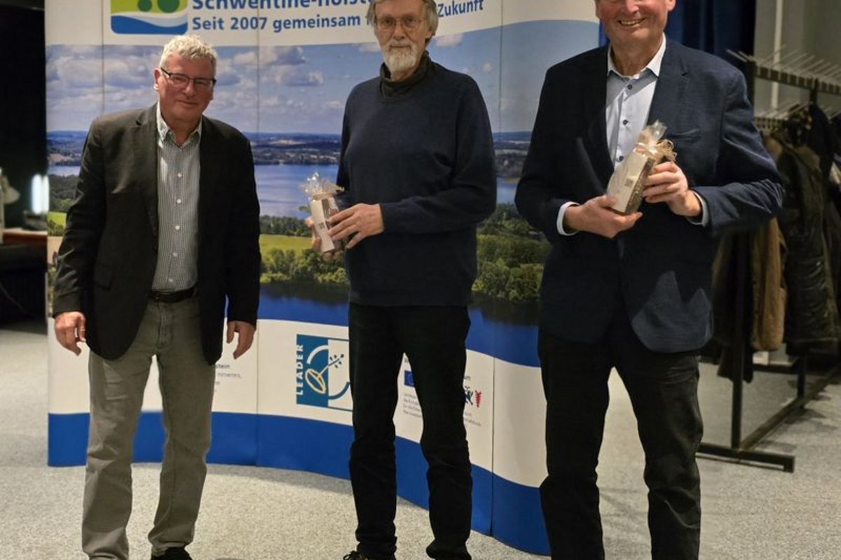 Drei Männer stehen vor einem Banner der LAG AktivRegion Schwentine-Holsteiner Schweiz und halten jeweils ein verpacktes Geschenk in der Hand